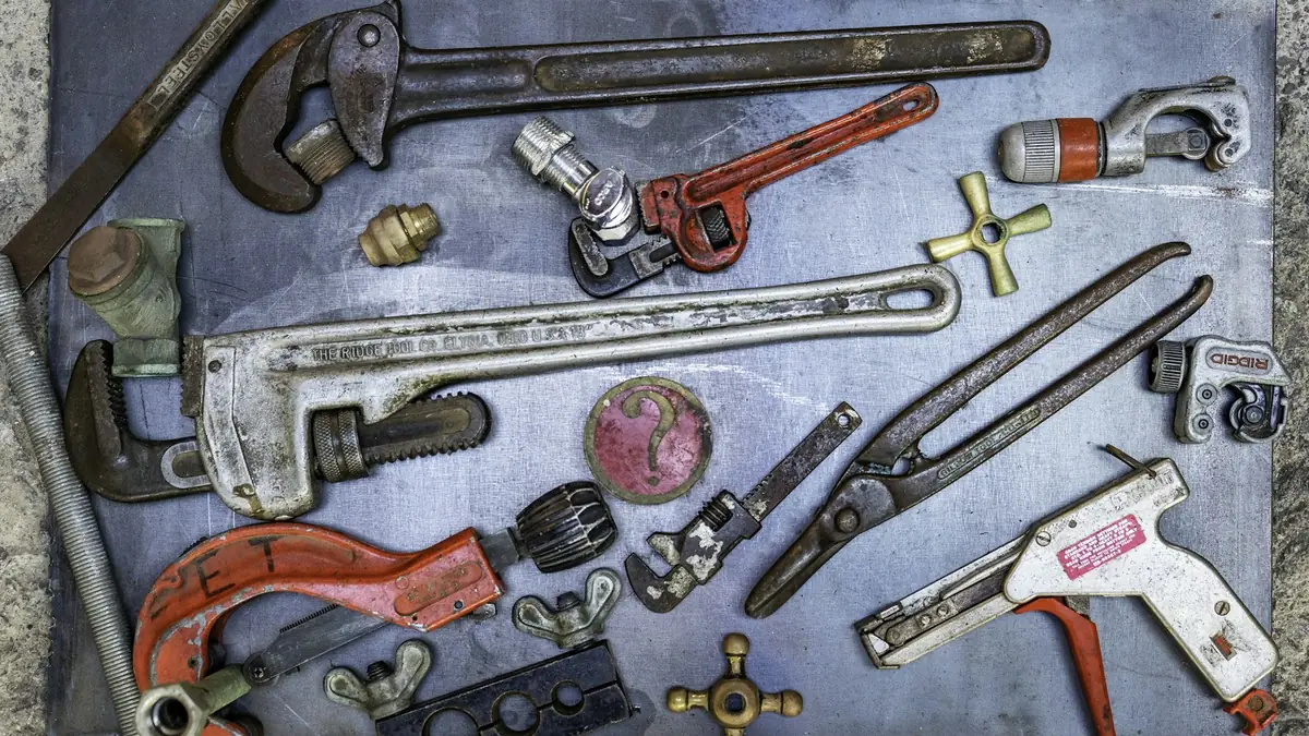 Pipe wrenches, cutters and fittings laid out on a workbench